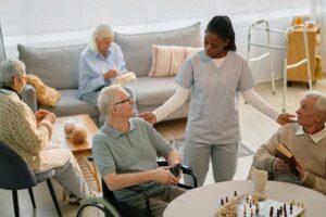 An older adult receives help taking medication from a caregiver in a comfortable living room setting.
