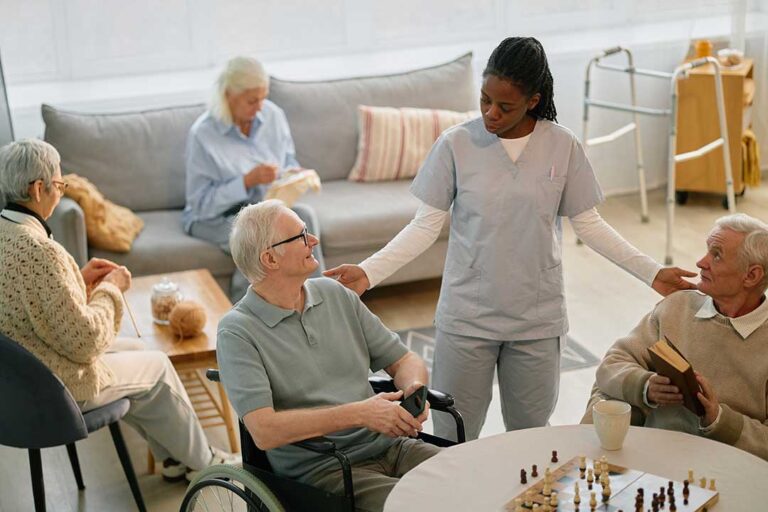 An older adult receives help taking medication from a caregiver in a comfortable living room setting.