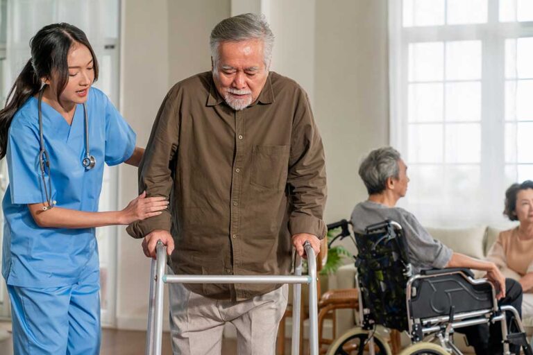 Older adults practice gentle chair exercises with an instructor in a bright assisted living activity room.